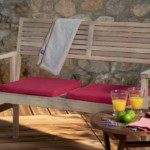 Coussins en toile de coton rouge, serviette en éponge coloris ficelle, essuie-main nid d'abeille rouge Les accessoires réalisés par Cécile Créations fabricantes de linge de maison sont disposés ur un banc en bois éclairé par un rayon de soleil